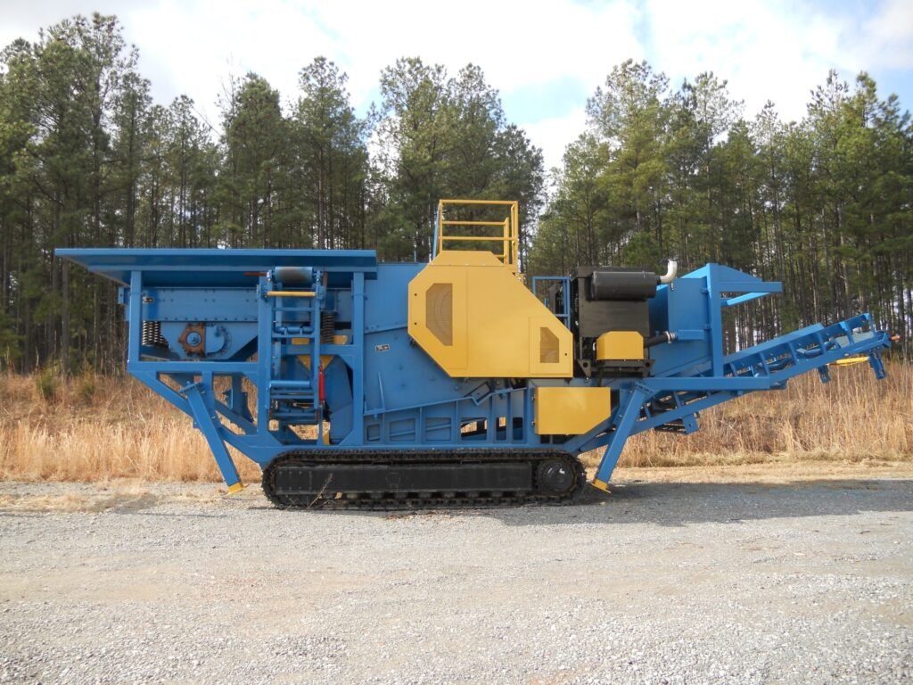 A large, industrial mobile crusher rests on gravel ground, featuring blue and yellow metal components.